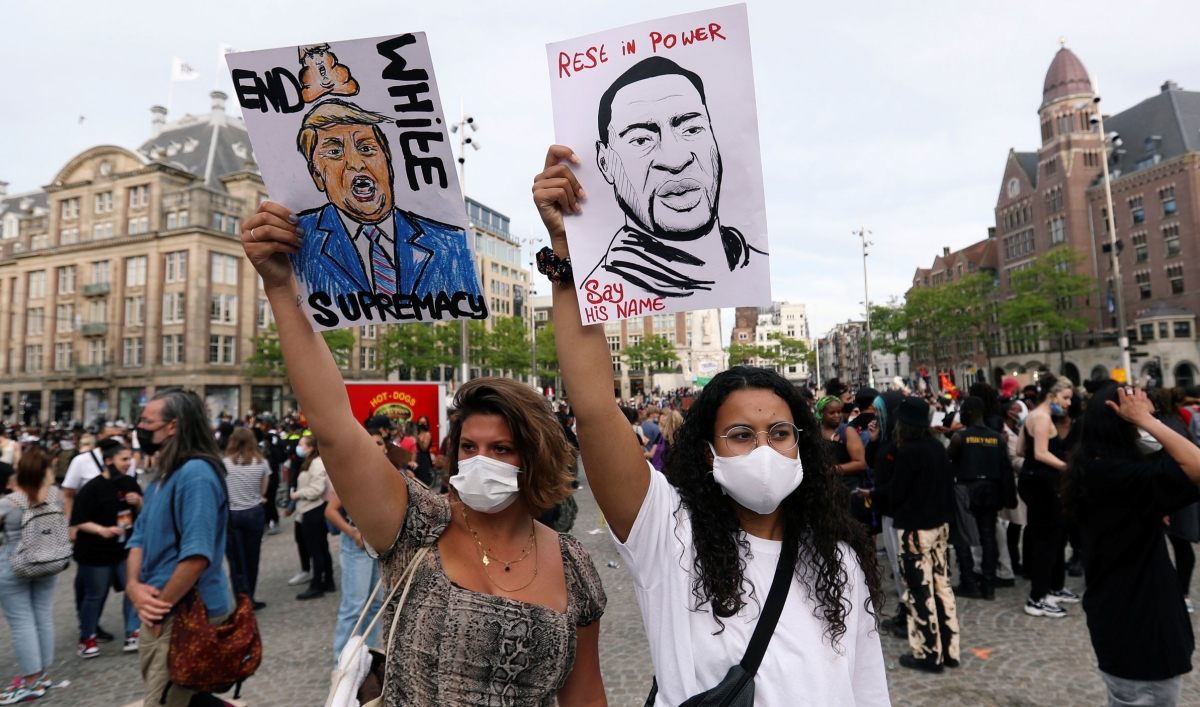 Women hold up a poster of US President Donald Trump reading "End white supremacy" and George Floyd reading "Rest in power. Say his name"