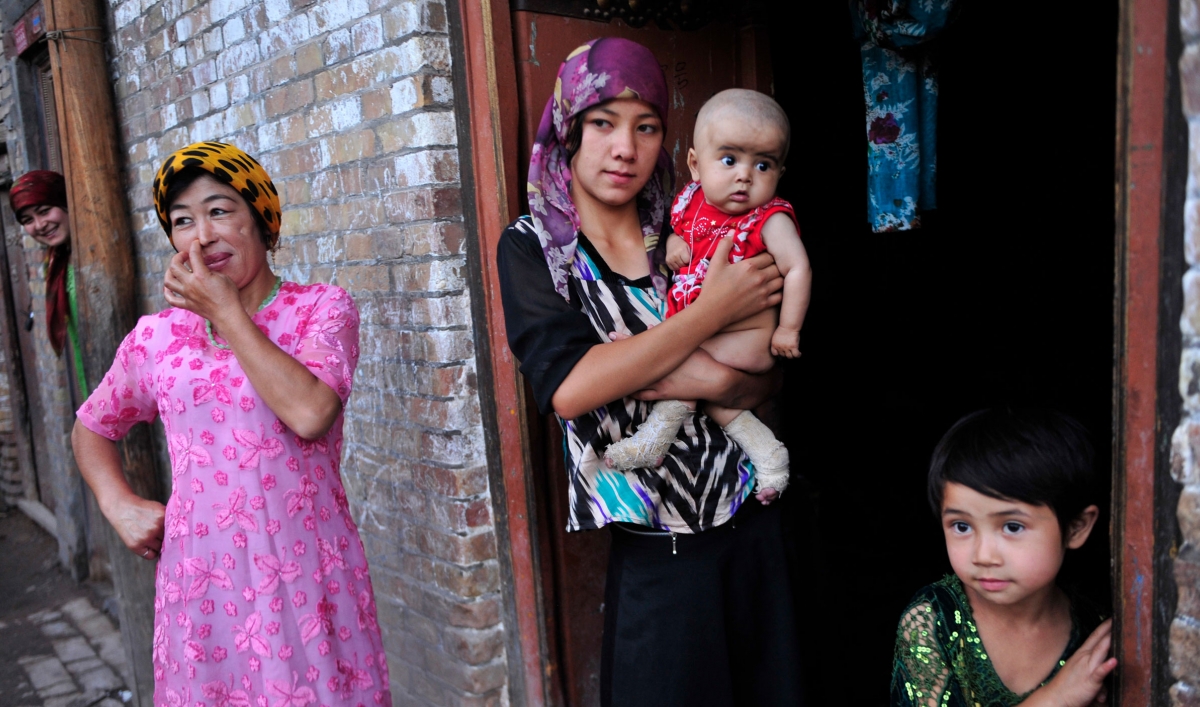 An ethnic Uighur woman hugs her son as she stands outside her house with her daughter and neighbors
