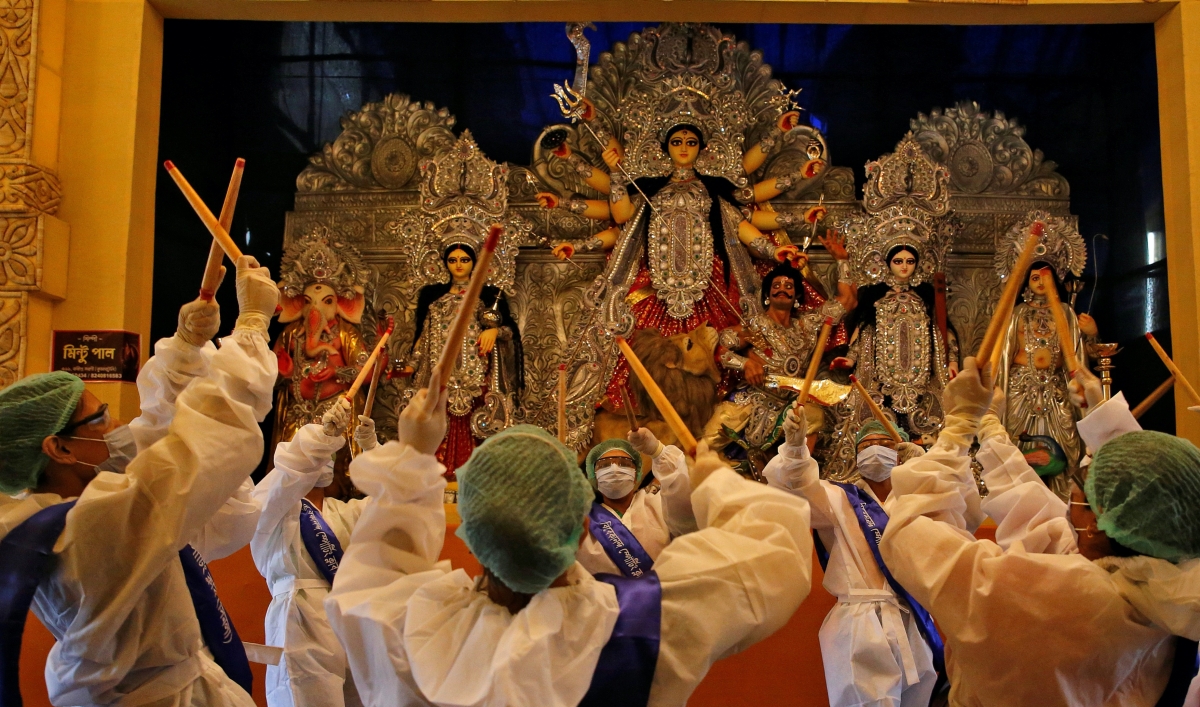 People wearing protective gear worship in front of a 10-armed ornate goddess idol on a platform.