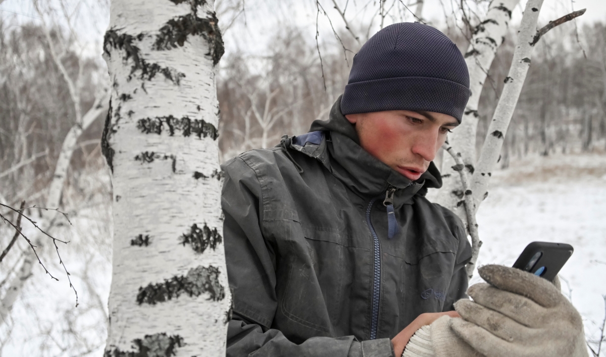 A young man wearing a jacket, a hat and gloves looks at his cellphone