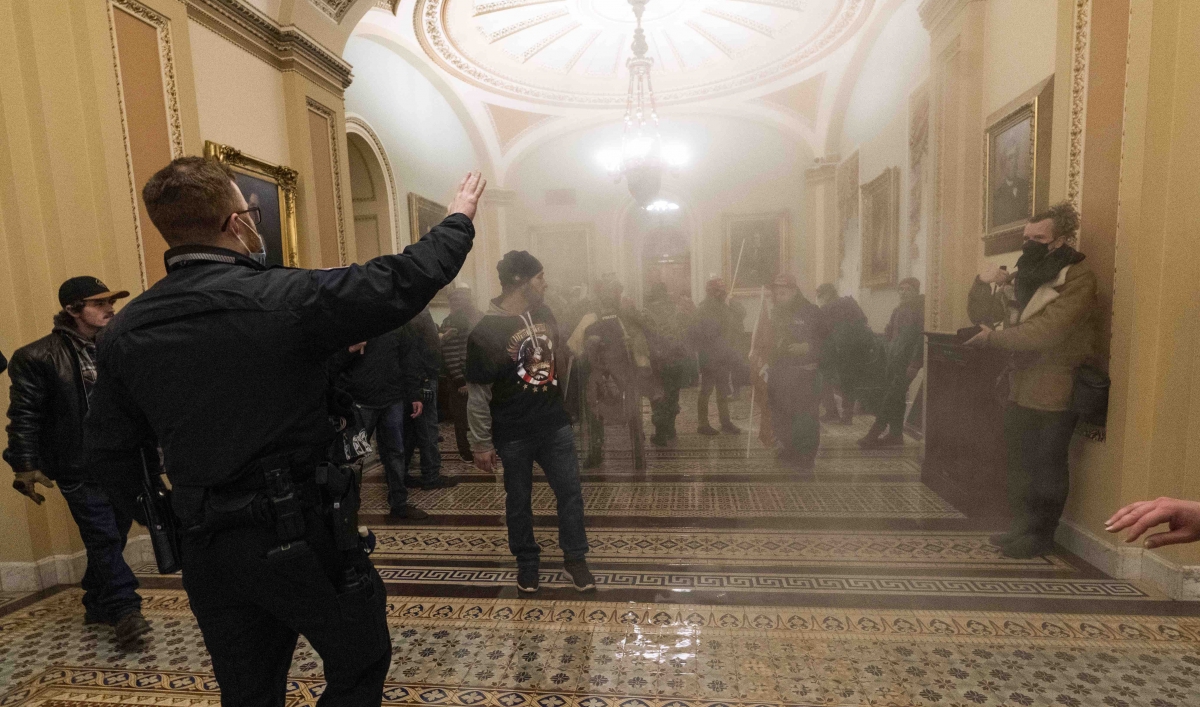 Smoke fills the walkway outside the Senate chamber as supporters of President Donald Trump are confronted by US Capitol Police officers inside the Capitol, Wednesday, Jan. 6, 2021, in Washington, DC.