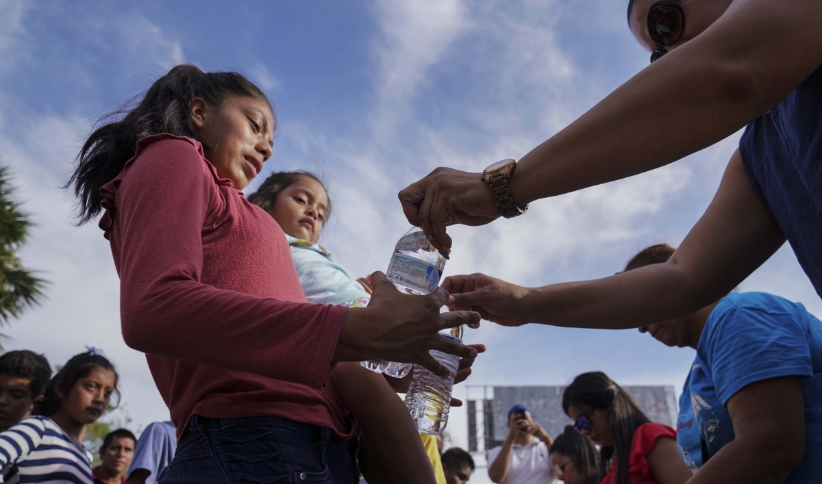 n this Aug. 30, 2019, photo, migrants, most who were returned to Mexico under the Trump administration’s “Remain in Mexico” program, receive bottles of water given by volunteers in an encampment near the Gateway International Bridge in Matamoros, Mexico.