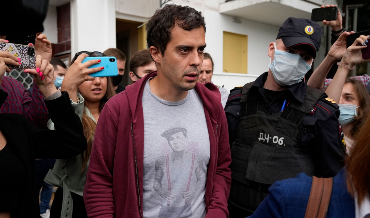 A man wearing a red cardigan with dark hair walks near a police officer.