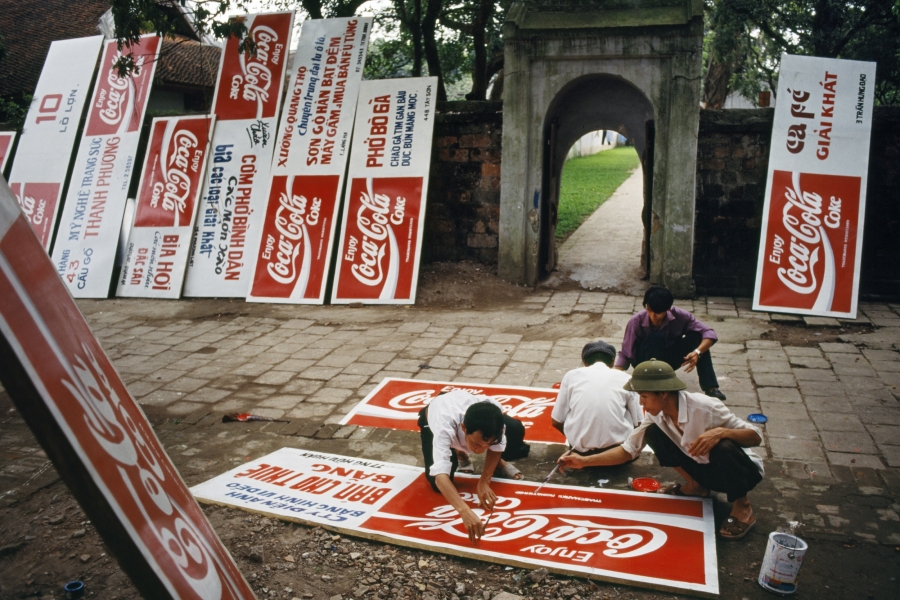 A group of men painting Coca-Cola logos on a dozen signboards. In the 1990s Vietnam revised its constitution to allow the practice of “private capitalism."