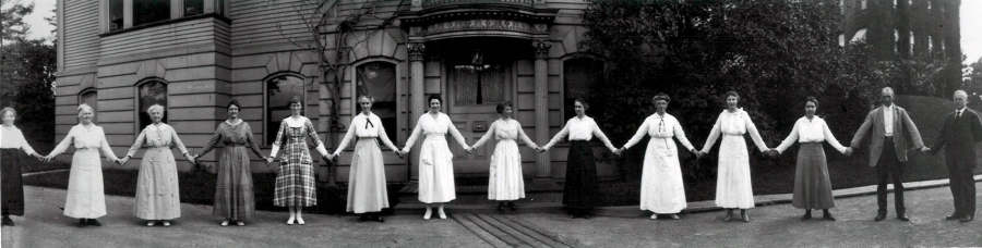 A dozen women hold hands in front of a building on the Harvard campus in 1918. They are all women "computers" working in the Harvard College Observatory. At the far right of the image is Edward Pickering, the head of the Observatory who hired them all.