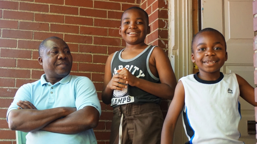 Man with folded arms looks at two smiling young boys, in front of door