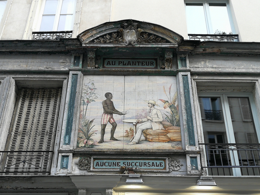 A 19th century street sign in 21st century Paris depicts a slave serving a drink to a white plantation owner. A 19th century street sign in 21st century Paris depicts a slave serving a drink to a white plantation owner.