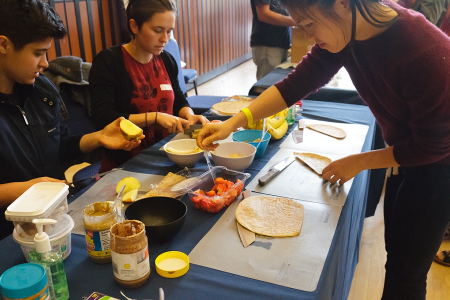 Woman making food at table, to others sitting at table looking on