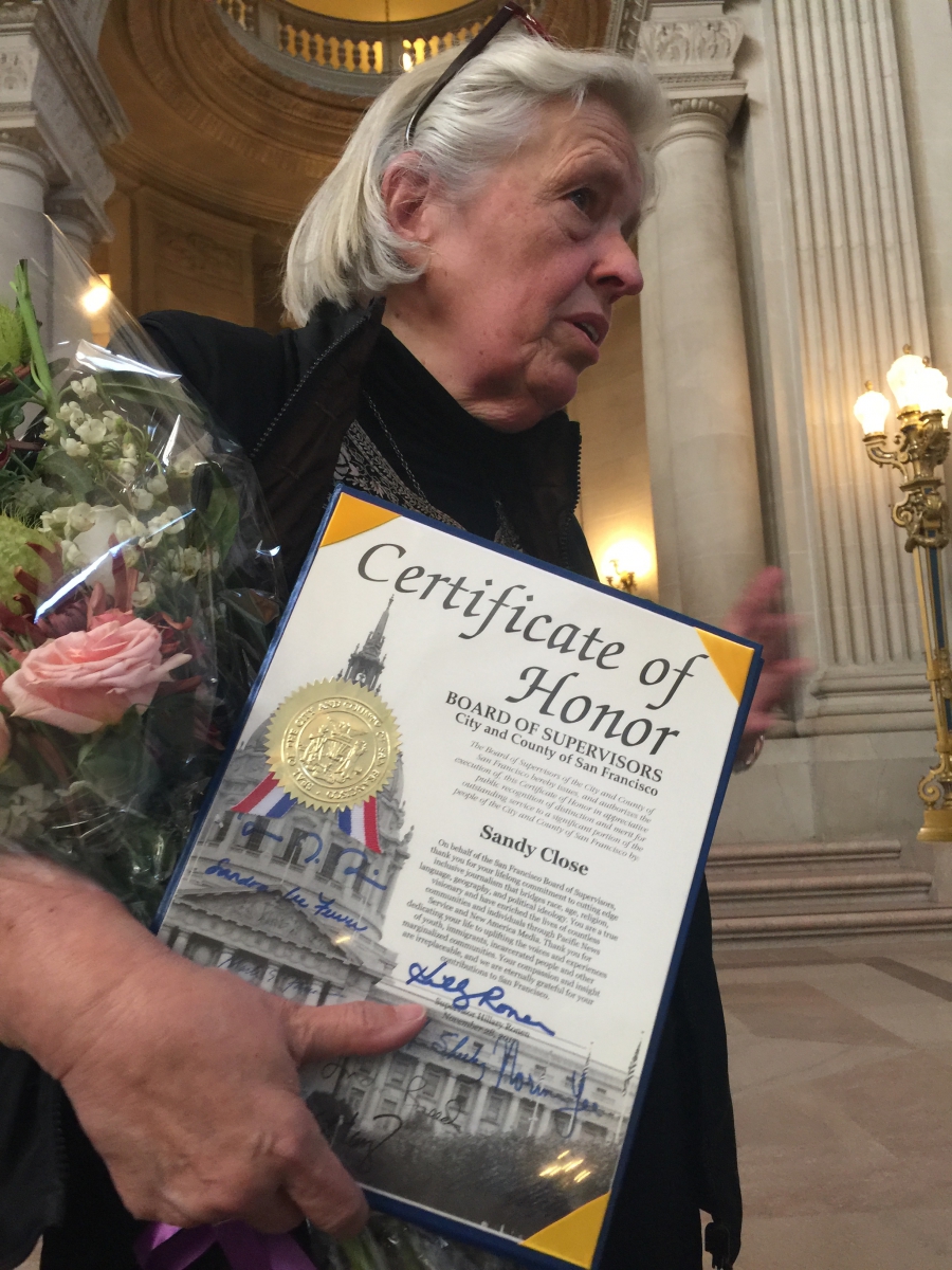 Woman stands with certificate, flowers behind