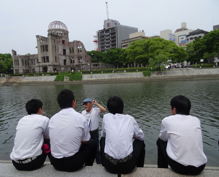 A volunteer guide speaks to school students across the river from the Atomic Bomb Dome in Hiroshima's Peace Memorial Park. A volunteer guide speaks to school students across the river from the Atomic Bomb Dome in Hiroshima's Peace Memorial Park.