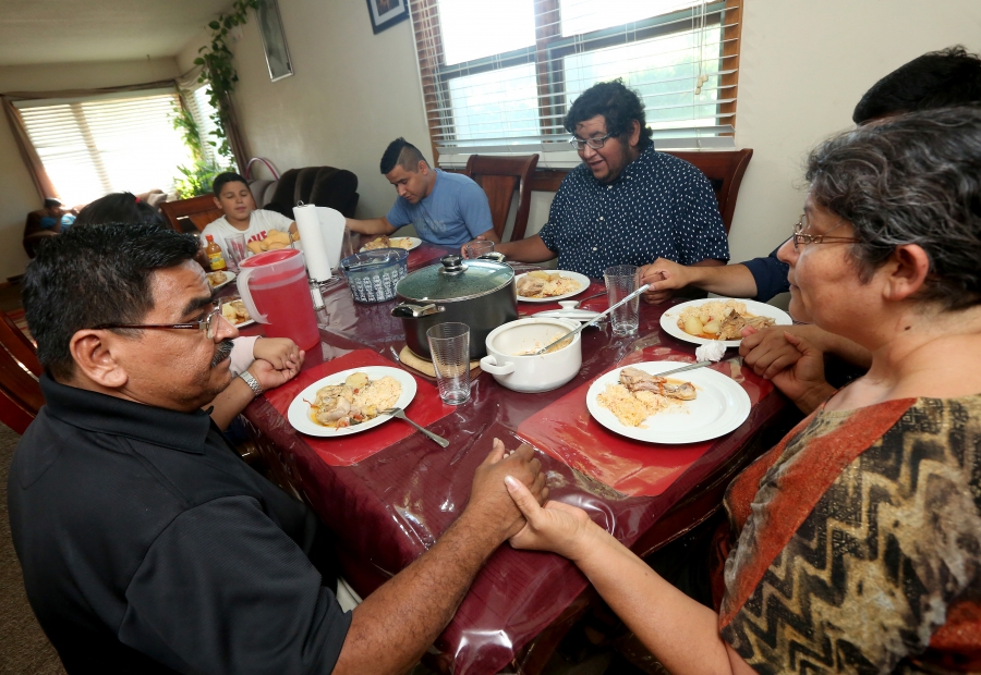 Family around table holds hand with heads bowed