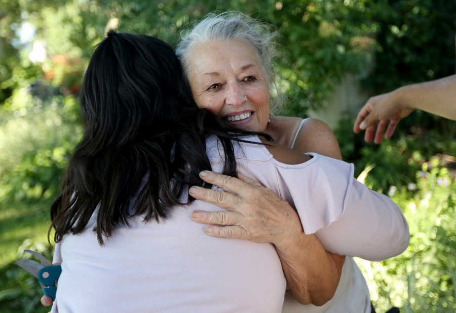 Young girl, seen from back, hungs woman while outdoors among greenery