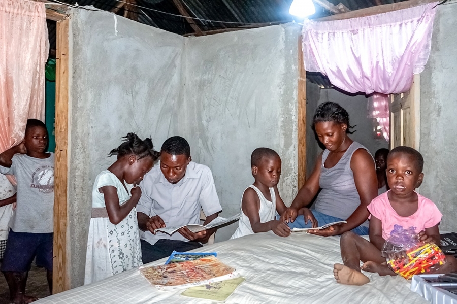Frantzy Monfilston, a teacher who lives with his family of four in Chansolme, helps his children finish their homework. Before Monfilston became a beneficiary of “Ma Maison Eclairée” in May 2017, he says, his home had no electricity.