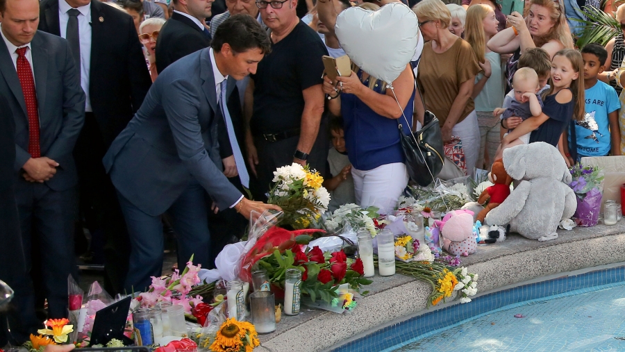 Canada's Prime Minister Justin Trudeau lays flowers at the site of a mass shooting. Around him is a large crowd assembled for a vigil.