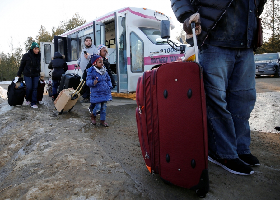 A line of people with suitcases exit a bus