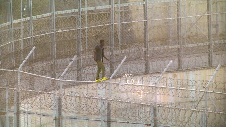 an african migrant scales a razor-wire topped fence in Ceuta, Spain