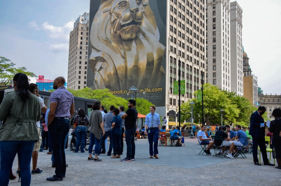 Downtown Detroit during a weekday at lunch time. People are shown sitting at outdoor tables and standing in line for a food truck in downtown Detroit.