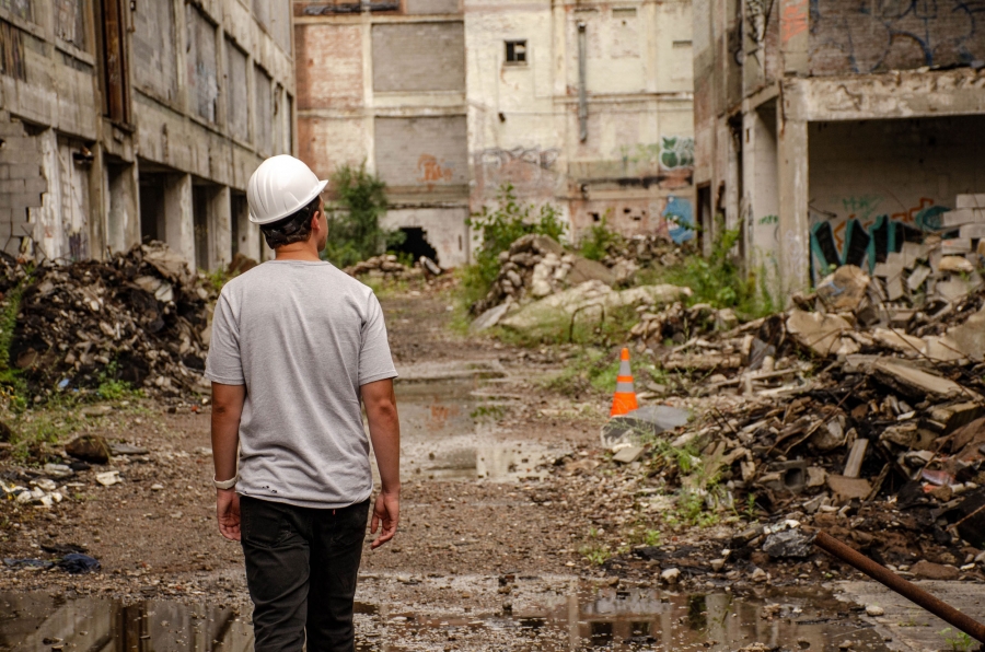 Jacob Jones from Pure Detroit gives tours through the debris and rubble of the former Packard Plant. Jacob Jones is shown from behind in a hard hat walking through the debris and rubble of the former Packard Plant.