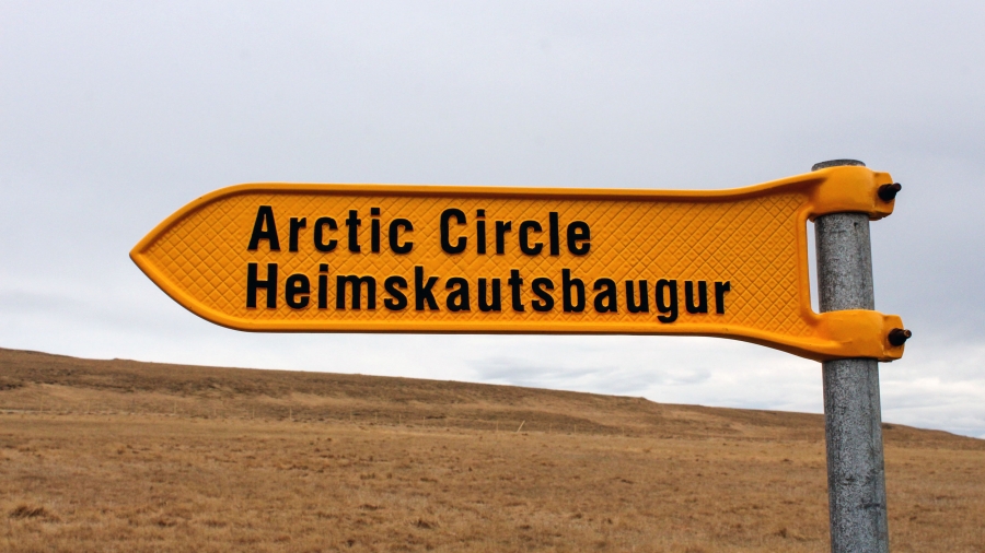 A yellow metal sign with the words "Arctic Circle" written in black points the way to the Arctic Circle on a tiny Icelandic island.