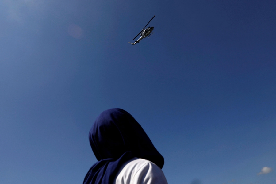 A Central American migrant, part of a caravan trying to reach the US, looks to helicopter as he waits to open the gate on the bridge that connects Mexico and Guatemala in Ciudad Hidalgo, Mexico, Oct. 21, 2018. A Central American migrant is shown looking up as a military helicopter flies overhead.