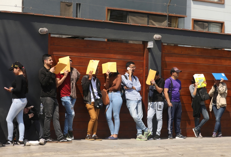 Venezuelan migrants wait in line outside the Interpol headquarters in Lima, Peru, Oct. 30, 2018. Venezuelan migrants are shown standing in line, many holding manila envelops, to get the needed paperwork for a temporary residency permit in Lima, Peru.