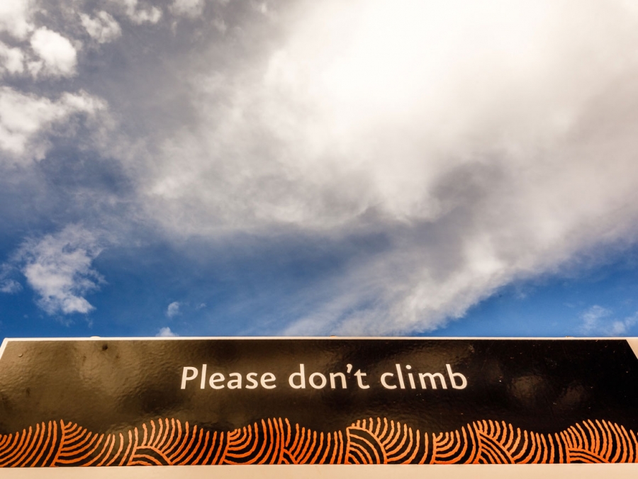 Signage at the base of Uluru implores visitors not to climb the rock. Climbing Uluru is offensive to local Aboriginal owners. Signage at the base of Uluru reads, 'please don't climb.'