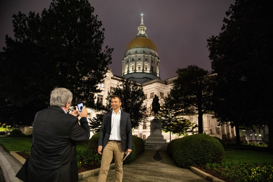 a man in a jackets and slacks get's his photo taken in front of the Georgia state capitol building