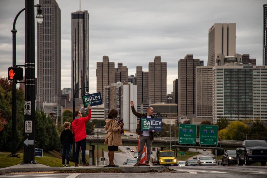 A group of people hold "Charlie Bailey for Attorney General" signs along the side of a road. The Atlanta skyline is behind them.