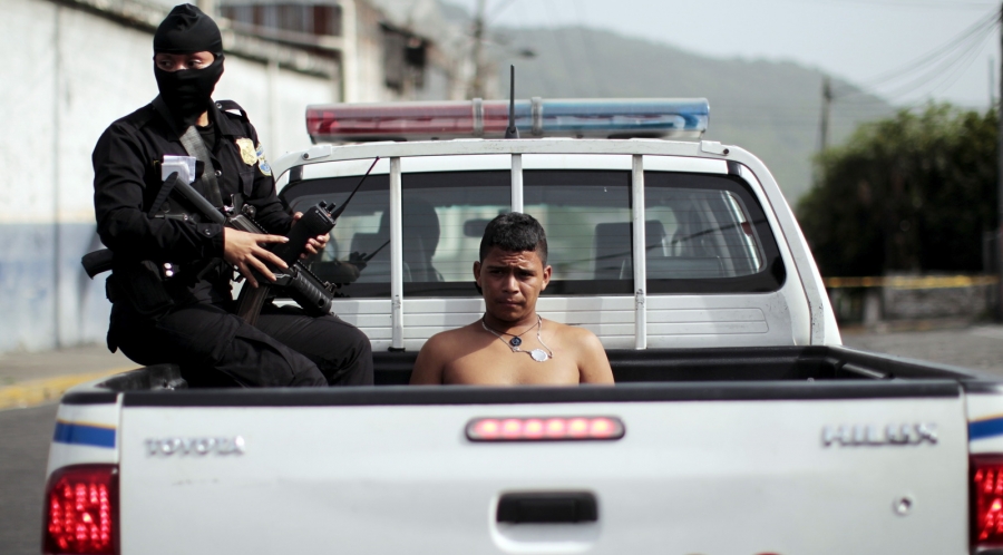 Salvadoran policewoman secures a suspected gang member during an anti-gang search operation in San Salvador, June 21, 2015. The Salvadoran Police and Army participated in a search operation in response of a deadly attack where two soldiers were killed by Policewoman in black mask with gun detains shirtless youth sitting in back of police pick-up truck.
