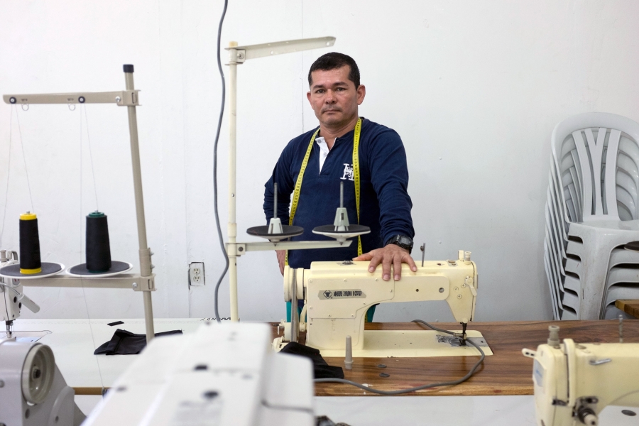 Diosenel Criado used to sew thousands of uniforms for FARC fighters during the war as an insurgent. Now he teaches ex-combatants to sew so they can make a new living. A man poses next to a sewing machine.