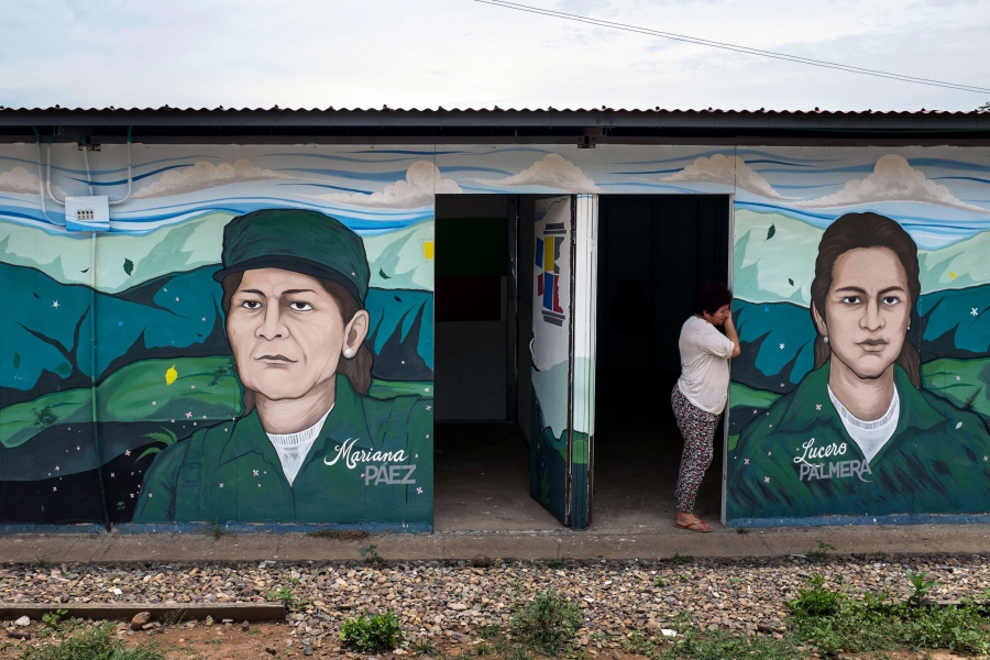 Ex-fighter Elisa Castro stands in an entrance of the FARC's memory museum at the Pondores reintegration camp in La Guajira, Colombia. A woman leans in the doorway of a building with images of FARC leaders painted on the outside.