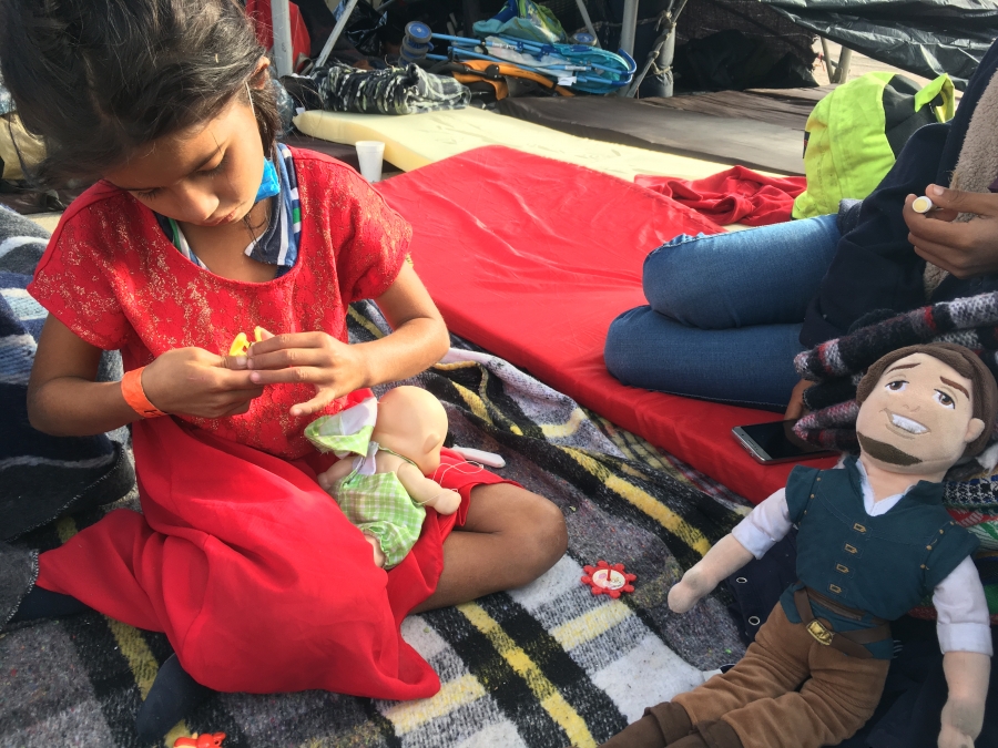 A little girl in a red dress plays with a doll on a blanket