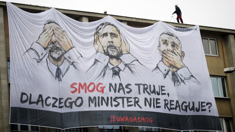 Greenpeace activists install a large banner featuring images of Poland's Environment Minister Maciej Grabowski and the slogan "Smog poisons us, why minister does not react?" a large banner hangs from a government building with cartoon images of a politician with his eyes, ears and mouth covered.