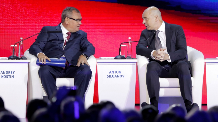 Two men sit in chairs. Behind them is a bright red background.