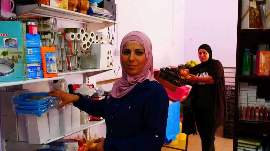 Sisters Fardous Zaki Silhiya, left, and Nihaya Yusuf Abu Aarad, run shops side by side in Am'ari refugee camp and hold opposite views on whether UNRWA's work should continue. Two women stand in a shop and look at the camera.