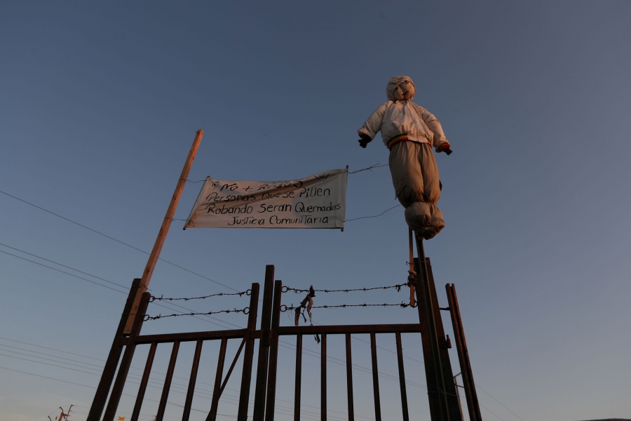 An effigy hangs at a fence with a banner reading “No more robberies. People caught stealing will be burned. Community justice.” A stuffed effigy is shown hangs at a fence with barbed wire and a sign reading “No more robberies. People caught stealing will be burned. Community justice.”