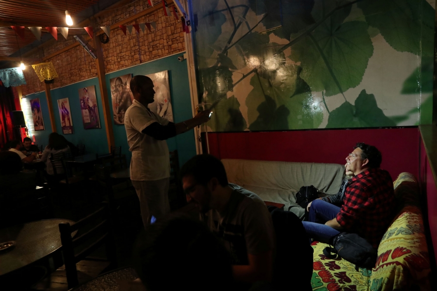 Venezuelan migrant Enrique Miller (44) takes a picture of customers at a restaurant. In this darkly lit restaurant, Venezuelan migrant Enrique Miller takes a picture using a flash.