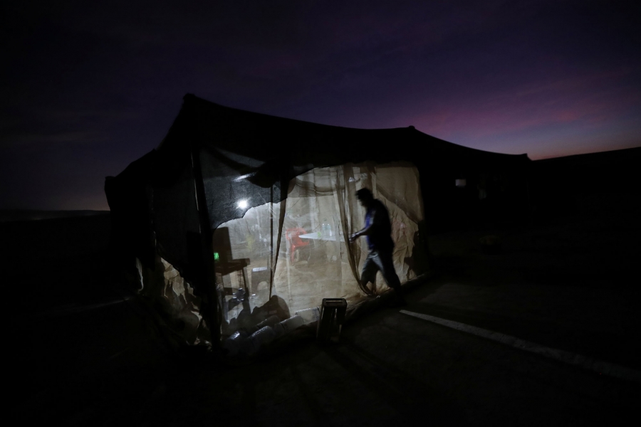 Undocumented Bolivian migrant known as Ramiro, 39, arrives at the camp where he works. In this photo taken at night, a stand-up, mesh net-walled tent is shown lit from the inside.
