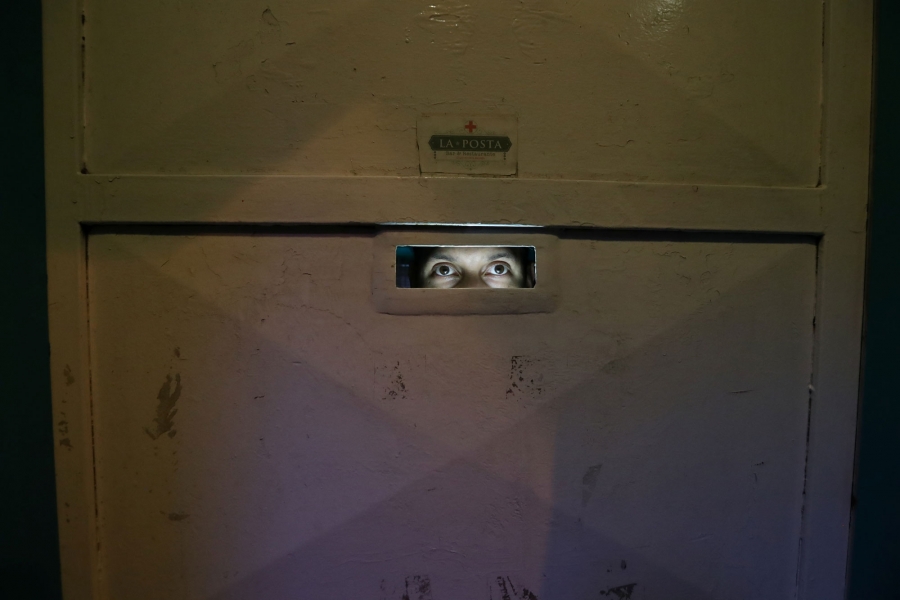Venezuelan migrant Angel Torres, 34, controls access to La Posta restaurant where Venezuelan migrants work. Venezuelan migrant Angel Torres is shown looking through a peep hole at La Posta restaurant.