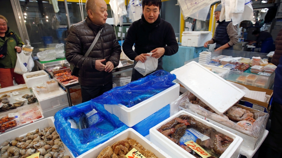 Masatoshi Fukutsuna, chef and owner of sushi restaurant Eiraku, chats with a wholesaler at Toyosu Fish Market in Tokyo, Japan, Dec. 11, 2018. Two men stand near fish in bins at fish market.