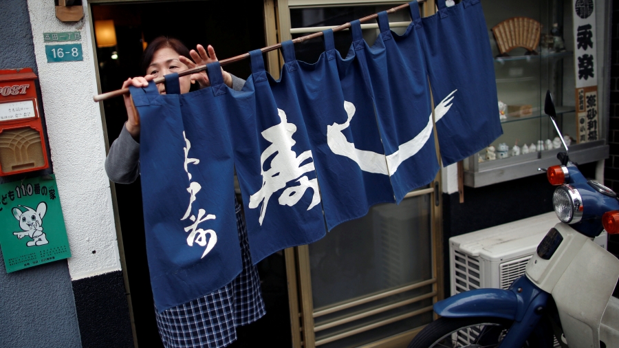 Mitsue Fukutsuna, the wife of sushi chef Masatoshi Fukutsuna, prepares for the opening of their restaurant Eiraku in Tokyo, Japan, Dec. 11, 2018. A woman moves a blue curtain with Japanese script as she opens the restaurant.