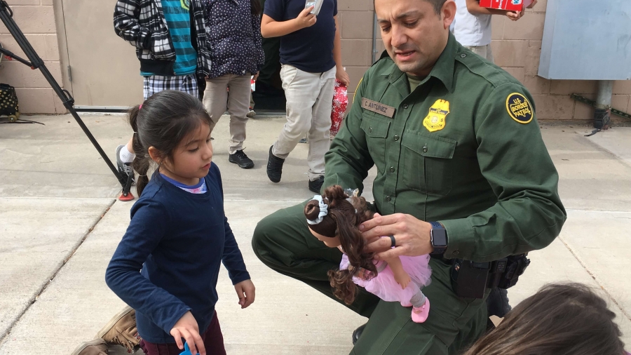 Border Patrol agent Carlos Antunez helps a young girl dress a doll outside Chihuahuita's community center. Border patrol agent helps a young girl dress a doll.