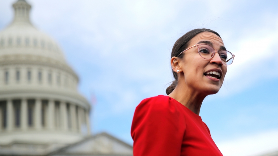 Democratic Representative-elect Alexandria Ocasio-Cortez of New York talks to reporters. Alexandria Ocasio-Cortez wears a red dress with Capitol building in background.