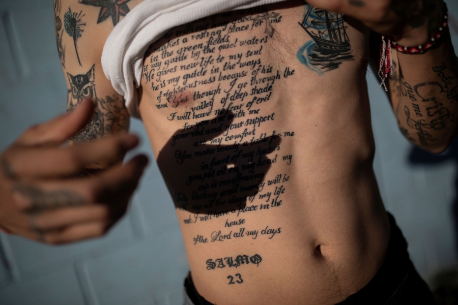 Juan Francisco, 25, from Honduras, shows his tattoo of the 23rd Psalm of the Book of Psalms. Juan Francisco is shown lifting his white shirt up to reveal a large tattoo of the 23rd Psalm of the Book of Psalms written out.