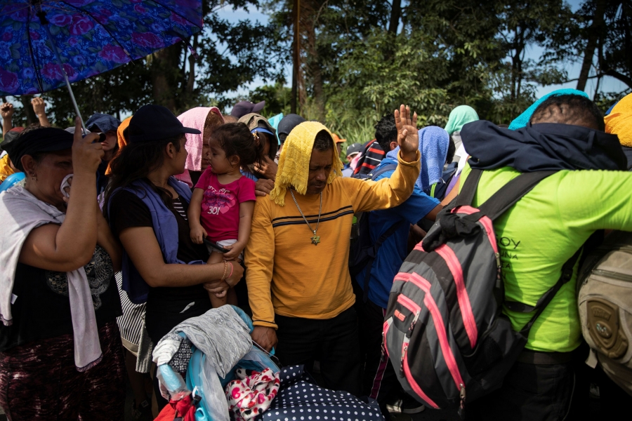Migrants pray as they are blocked by the Mexican police during an operation to detain them for entering the country, in Metapa. A group of migrants are shown crowded together outside praying in Metapa.