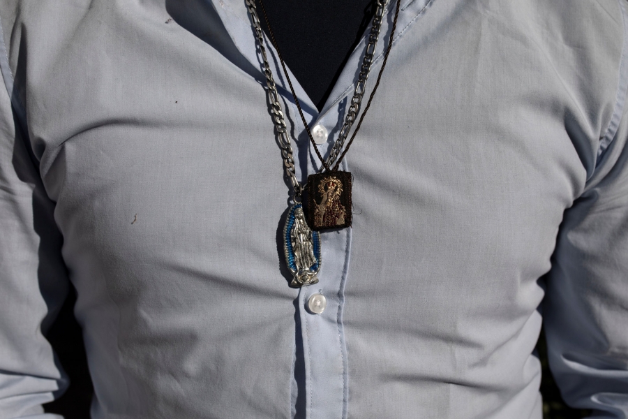 Victor Alfonso, 29, from Guatemala, wears charms depicting the Virgin of Guadalupe. In this close-up photograph, Victor Alfonso in a blue button down shirt, wears charms depicting the Virgin of Guadalupe.