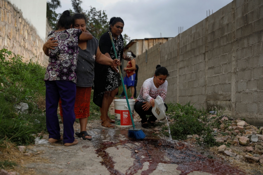 Relatives and friends of Ronald Blanco wash the blood from the crime scene. Relatives and friends of Ronald Blanco are shown in the street, a pair hugging and another wash the blood from the crime scene.