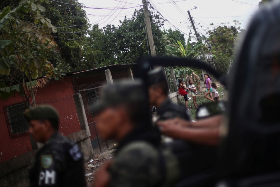 A group of children look toward a crime scene, where a man lies dead, after a shooting in San Pedro Sula, Honduras. A group of children are shown in the distance looking toward a crime scene with police in te near ground in soft focus.