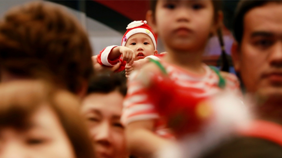 Child in Bangkok on Christmas A toddler is dressed up as Santa Claus and looks at the camera while looking over a crowd of people.