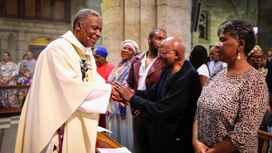 Desmond Tutu in Christmas service. Archbishop Emeritus Desmond Tutu shakes hands with priests inside a church.